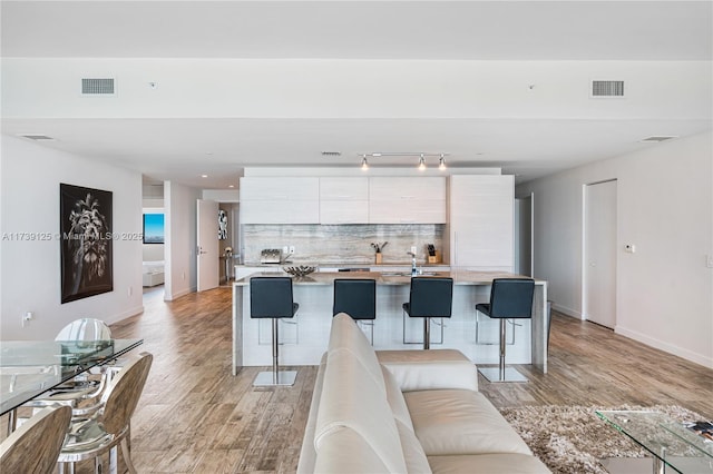 living room with light wood-style floors, visible vents, and baseboards