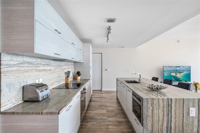 kitchen featuring sink, appliances with stainless steel finishes, an island with sink, decorative backsplash, and light wood-type flooring