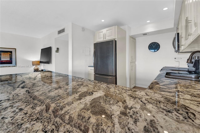 kitchen featuring appliances with stainless steel finishes, white cabinetry, sink, dark stone counters, and kitchen peninsula