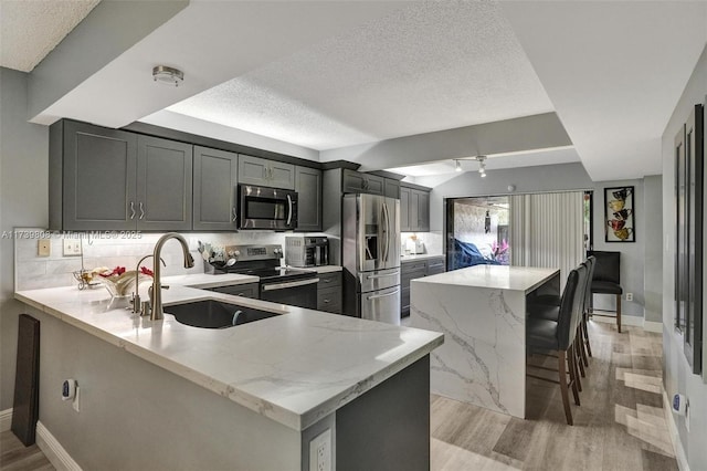 kitchen with sink, a breakfast bar area, light stone counters, appliances with stainless steel finishes, and kitchen peninsula