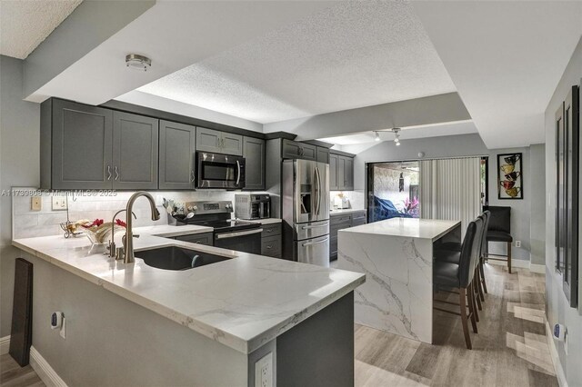 kitchen featuring light wood finished floors, a sink, a center island, a textured ceiling, and appliances with stainless steel finishes