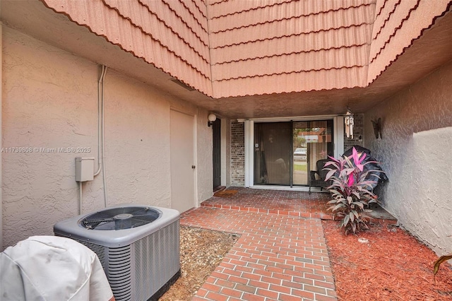 property entrance with cooling unit, a tile roof, and stucco siding