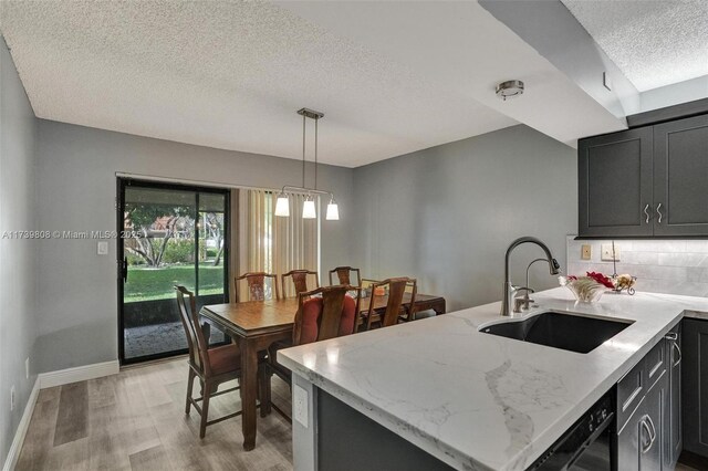 kitchen with tasteful backsplash, light stone counters, light wood-style floors, a sink, and a textured ceiling