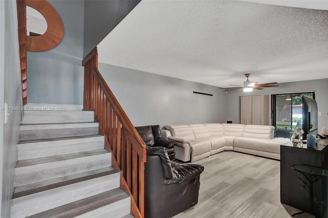 living room featuring a textured ceiling, ceiling fan, wood finished floors, and stairway