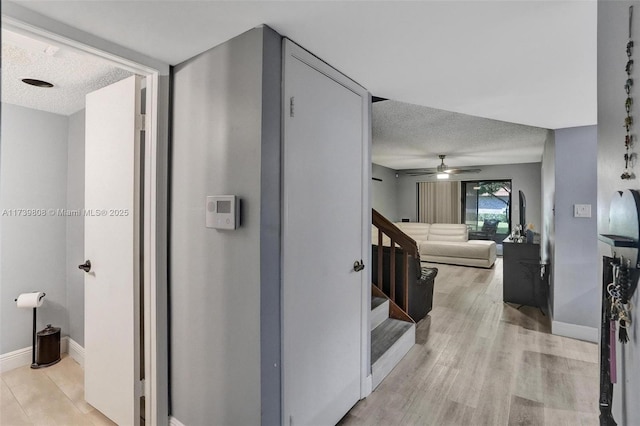 hall featuring a textured ceiling, stairway, light wood-style floors, and baseboards