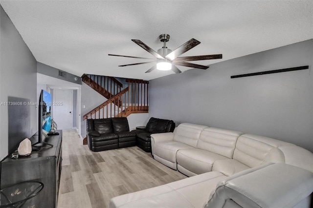 living room with a textured ceiling, a ceiling fan, stairway, and light wood-style floors
