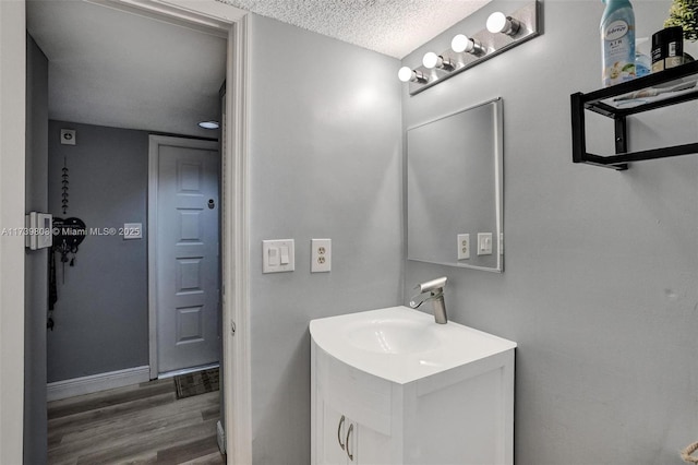 bathroom with vanity, a textured ceiling, wood finished floors, and baseboards