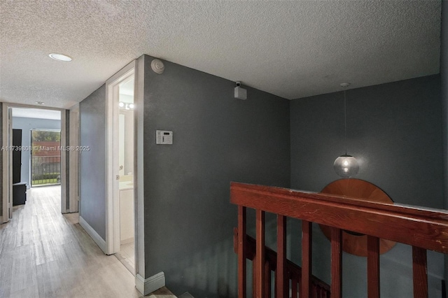 hallway with baseboards, a textured ceiling, and light wood-style flooring
