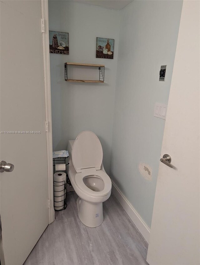bathroom with baseboards, wood finished floors, and toilet