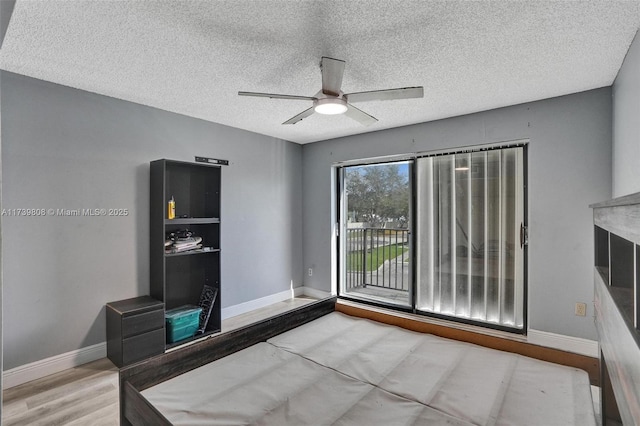 unfurnished bedroom featuring ceiling fan, access to outside, baseboards, a textured ceiling, and wood finished floors