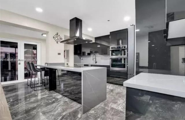 kitchen featuring island range hood, sink, a kitchen breakfast bar, stainless steel double oven, and french doors