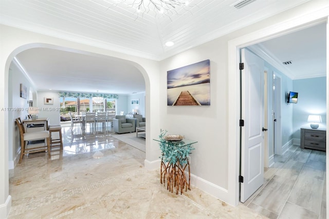 hallway with arched walkways, baseboards, visible vents, and crown molding