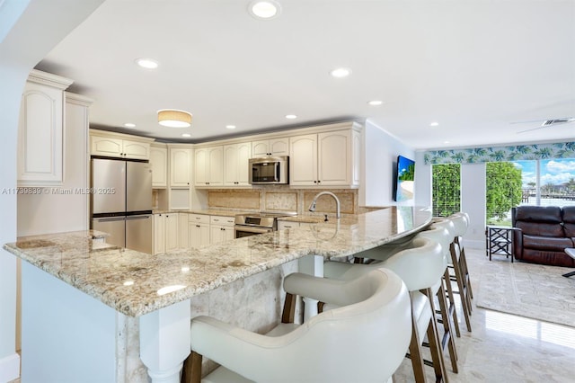 kitchen with appliances with stainless steel finishes, a peninsula, and light stone counters