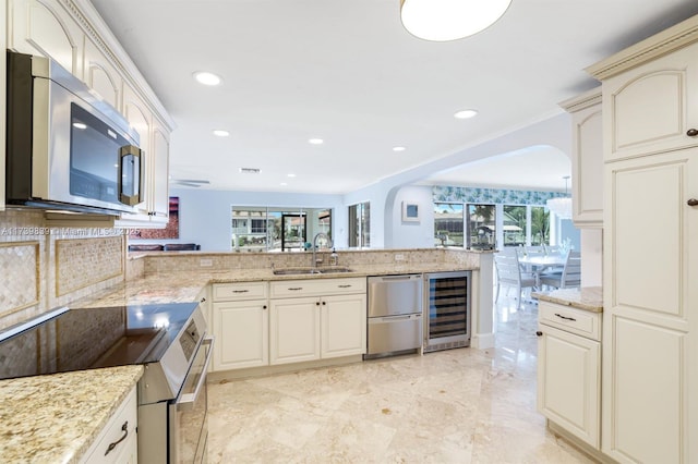 kitchen with arched walkways, stainless steel appliances, a sink, beverage cooler, and a peninsula