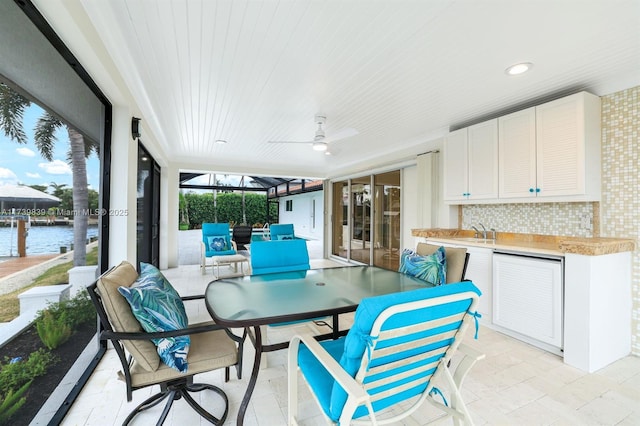 sunroom / solarium with a water view, a sink, and a ceiling fan