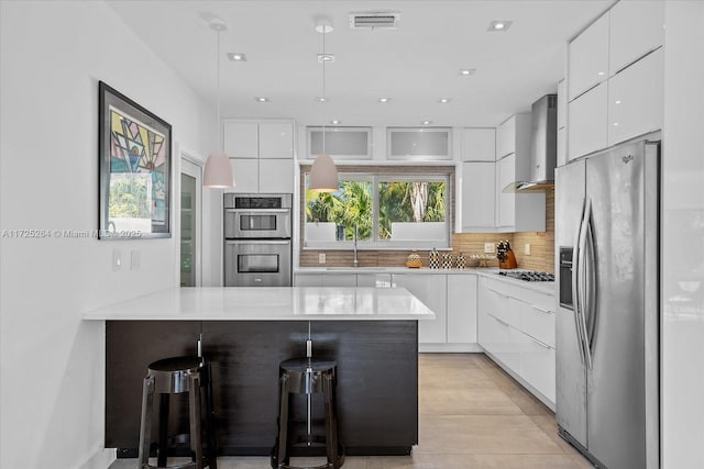 kitchen featuring white cabinetry, appliances with stainless steel finishes, a breakfast bar area, and wall chimney range hood