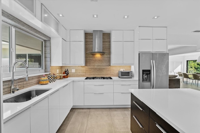 kitchen with wall chimney exhaust hood, sink, stainless steel fridge, white cabinets, and backsplash