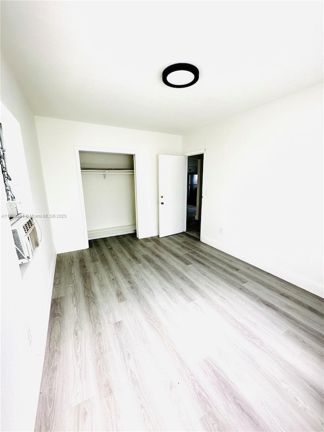 unfurnished bedroom featuring cooling unit, light hardwood / wood-style floors, and a closet