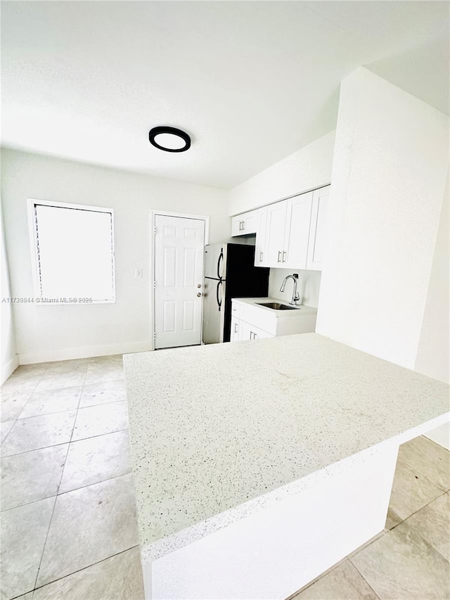 kitchen featuring sink, white cabinetry, light stone counters, refrigerator, and light tile patterned floors