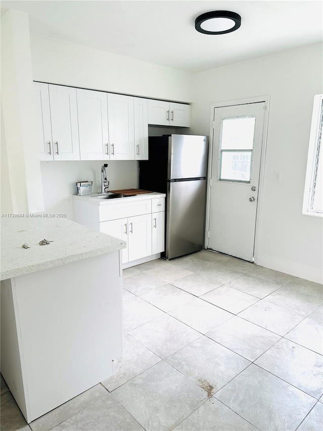 kitchen with white cabinetry, stainless steel fridge, light tile patterned flooring, and light stone counters