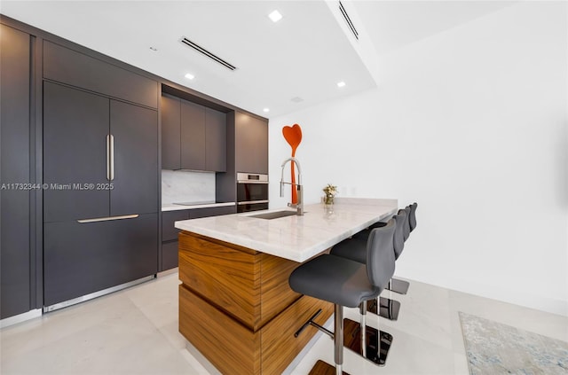 kitchen with sink, a kitchen breakfast bar, a center island, light stone countertops, and decorative backsplash