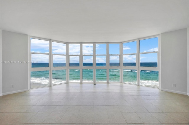 empty room featuring a water view, a wall of windows, a beach view, and a wealth of natural light