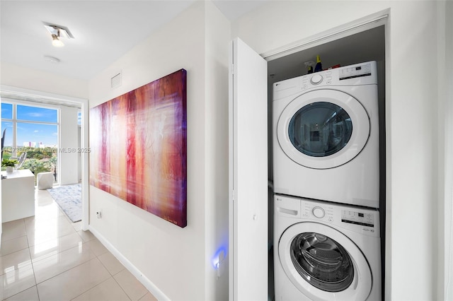 laundry area with stacked washer / drying machine and light tile patterned floors