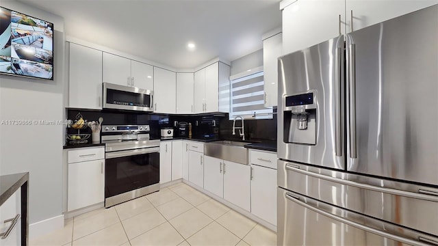 kitchen with sink, white cabinets, backsplash, light tile patterned floors, and stainless steel appliances