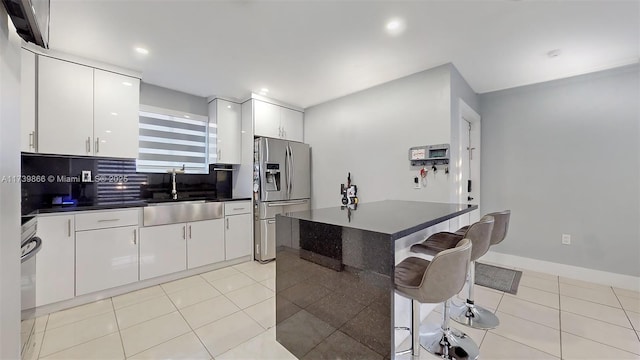 kitchen featuring light tile patterned flooring, a breakfast bar, white cabinetry, sink, and stainless steel fridge