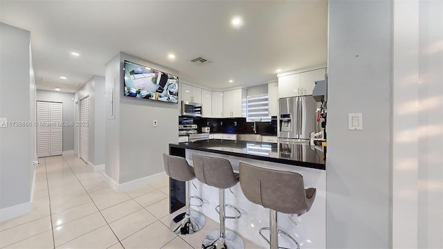 kitchen featuring light tile patterned flooring, a breakfast bar, white cabinets, stainless steel appliances, and backsplash