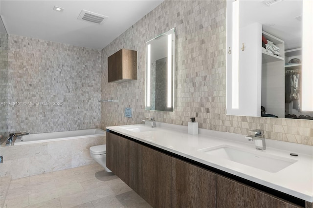 bathroom with toilet, tile walls, vanity, tiled tub, and backsplash