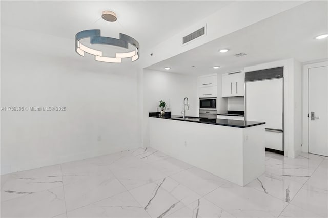 kitchen with white cabinetry, built in appliances, sink, and kitchen peninsula