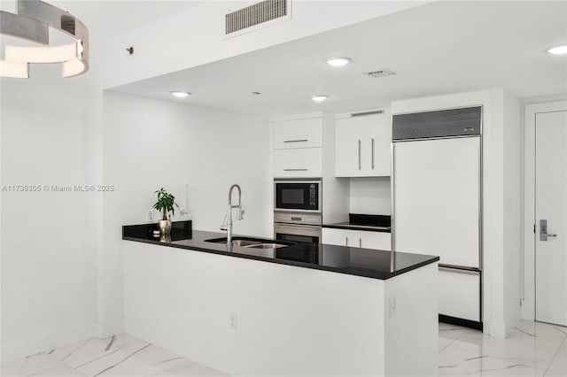 kitchen featuring built in appliances, kitchen peninsula, sink, and white cabinets