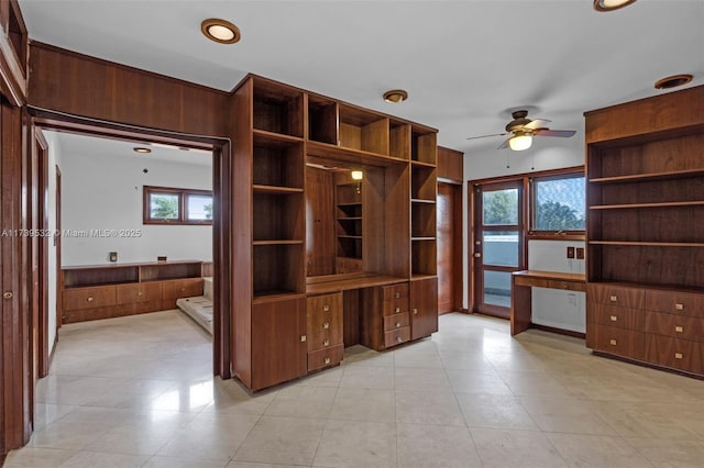 unfurnished office featuring light tile patterned floors, built in desk, and ceiling fan