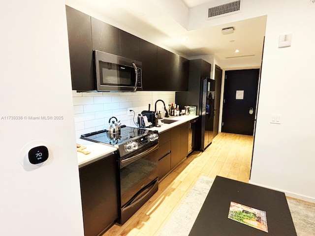 kitchen featuring backsplash, black appliances, sink, and light wood-type flooring