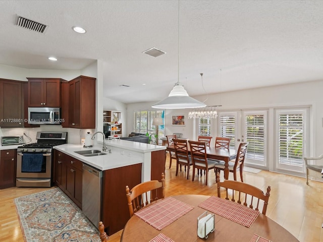 kitchen with sink, hanging light fixtures, light hardwood / wood-style floors, kitchen peninsula, and stainless steel appliances