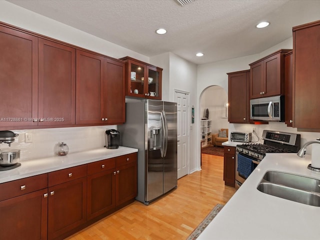 kitchen with sink, stainless steel appliances, tasteful backsplash, a textured ceiling, and light wood-type flooring