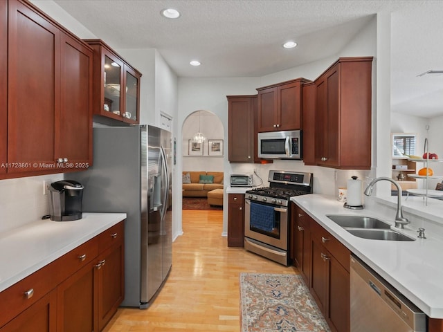 kitchen featuring sink, backsplash, stainless steel appliances, a textured ceiling, and light wood-type flooring