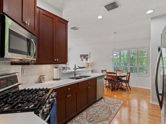 kitchen featuring sink, tasteful backsplash, hanging light fixtures, appliances with stainless steel finishes, and light hardwood / wood-style floors