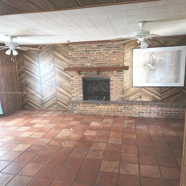 unfurnished living room with wooden walls, ceiling fan, tile patterned floors, and a fireplace