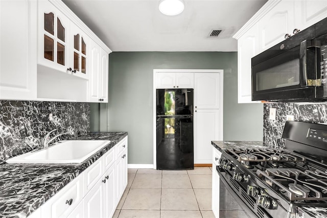 kitchen featuring sink, white cabinets, dark stone counters, light tile patterned floors, and black appliances