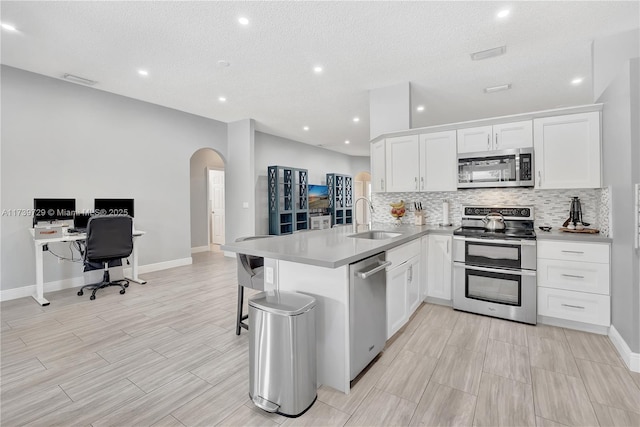 kitchen with sink, white cabinetry, stainless steel appliances, decorative backsplash, and kitchen peninsula