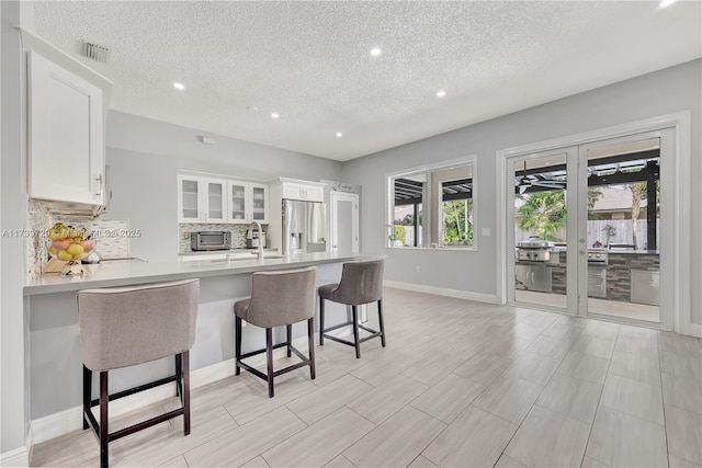 kitchen featuring french doors, white cabinetry, stainless steel fridge with ice dispenser, a kitchen breakfast bar, and kitchen peninsula