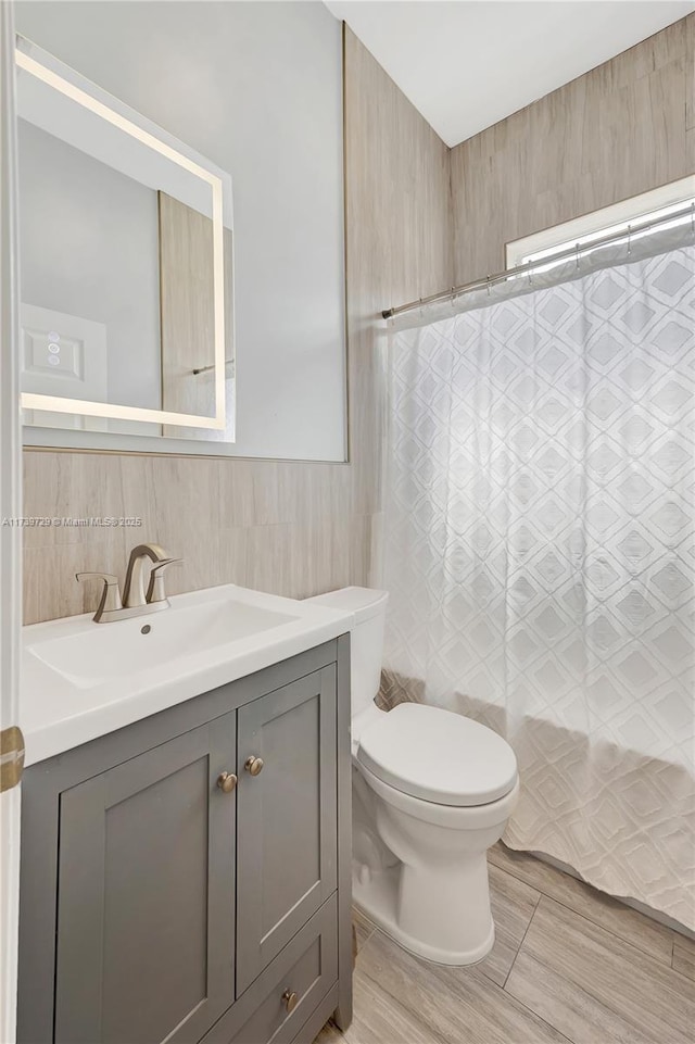 full bathroom with vanity, tile walls, shower / bath combo with shower curtain, and toilet