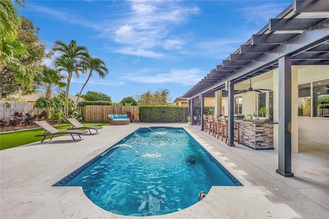 view of swimming pool with pool water feature, a patio area, ceiling fan, and a bar