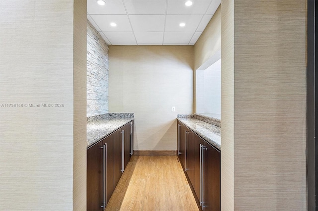 bar with light stone countertops, a drop ceiling, dark brown cabinetry, and light hardwood / wood-style flooring