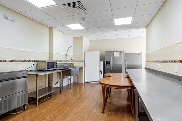 kitchen with a paneled ceiling, backsplash, stainless steel counters, light hardwood / wood-style floors, and stainless steel appliances