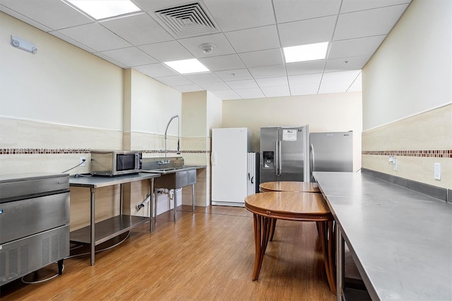 kitchen featuring a drop ceiling, stainless steel counters, light wood-type flooring, appliances with stainless steel finishes, and backsplash