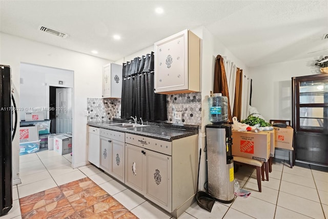 kitchen featuring a sink, dark countertops, visible vents, freestanding refrigerator, and backsplash