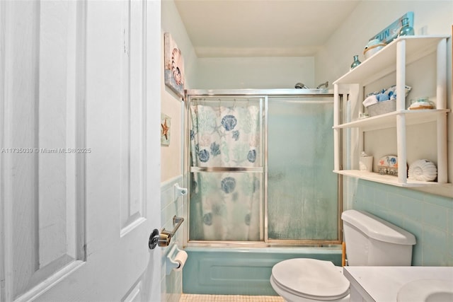 full bathroom featuring tile walls, toilet, combined bath / shower with glass door, and vanity